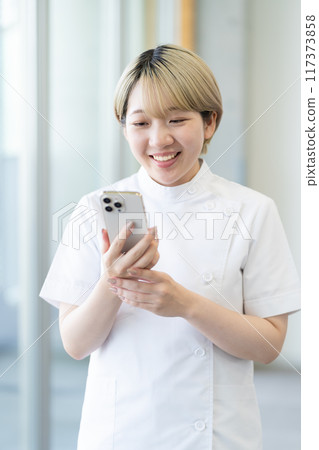 A young blonde short-haired chiropractor holding a smartphone (free hair color, work in your own way, work environment) A young blonde short-haired chiropractor holding a smartphone (free hair color, work in your own way, work environment) 117373858