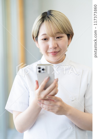 A young blonde short-haired chiropractor holding a smartphone (free hair color, work in your own way, work environment) A young blonde short-haired chiropractor holding a smartphone (free hair color, work in your own way, work environment) 117373860