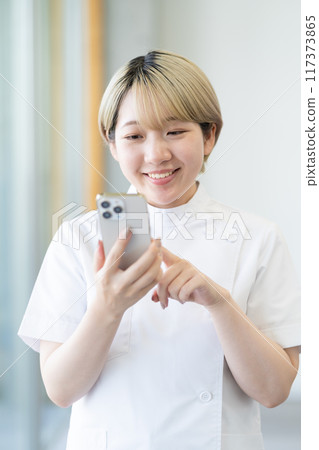 A young blonde short-haired chiropractor holding a smartphone (free hair color, work in your own way, work environment) 117373865