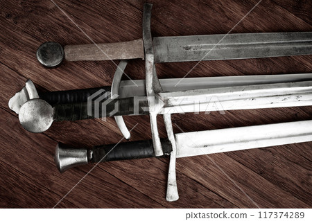 Medieval swords on wooden background. 117374289