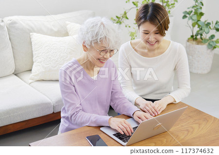 Mother and daughter using laptop in living room Mother and daughter using laptop in living room 117374632