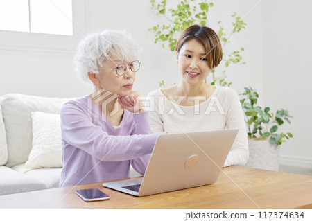 Mother and daughter using laptop in living room Mother and daughter using laptop in living room 117374634