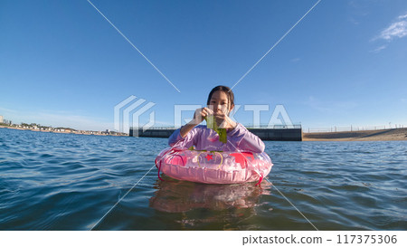 A young elementary school girl playing in the water with a swim ring at a midsummer beach 117375306