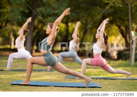 Group of girls practicing yoga at group session in sunny garden, performing Anjaneyasana, or Crescent Moon Pose Group of girls practicing yoga at group session in sunny garden, performing Anjaneyasana, or Crescent Moon Pose 117375899