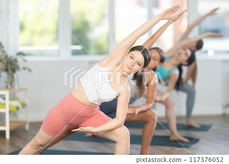Smiling young women training yoga positions in modern yoga gym Smiling young women training yoga positions in modern yoga gym 117376052