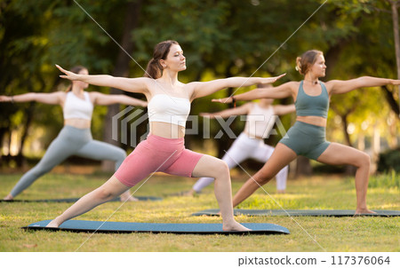 Happy women standing yoga pose and making full body stretching workout by female trainer in summer park 117376064