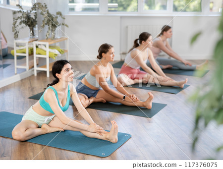 Girl teaches yoga lesson, shows students technique of performing Parivritta Janu Shirshasana asana 117376075