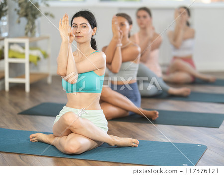 Young girl teaches yoga lesson, shows students technique of performing Gomukhasana asana 117376121