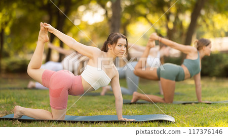 Yoga lesson visitors girls perform eka Padahastasana Marjariasana in park Yoga lesson visitors girls perform eka Padahastasana Marjariasana in park 117376146