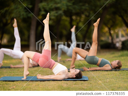 Yoga lesson visitors girls perform Setu Badha Sarvangasana in park 117376335