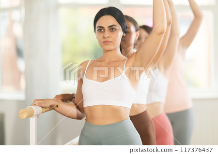 Young girl practicing third arm position holding by ballet barre Young girl practicing third arm position holding by ballet barre 117376437