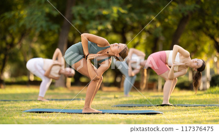 Yoga lesson visitors girls perform Parivritta Uttanasana in park Yoga lesson visitors girls perform Parivritta Uttanasana in park 117376475