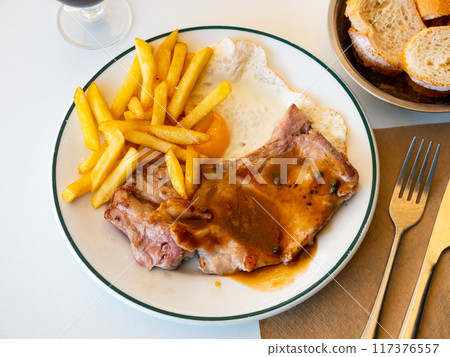 Two fried pork chops with bone, supplemented with slices of French fries, fried egg and bran bread Two fried pork chops with bone, supplemented with slices of French fries, fried egg and bran bread 117376557