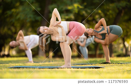 Fitness, sport and healthy lifestyle concept: girls doing yoga yoga pose - vrikshasana pose on mat in sunny summer park Fitness, sport and healthy lifestyle concept: girls doing yoga yoga pose - vrikshasana pose on mat in sunny summer park 117376593