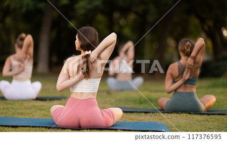 Yoga training in summer sunny park - girls in kagasana pose on mats Yoga training in summer sunny park - girls in kagasana pose on mats 117376595