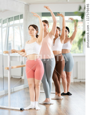 Young girl practicing third position holding by ballet barre 117376646