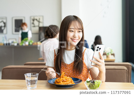 A young woman looking at her smartphone while eating lunch at a cafe 117377091