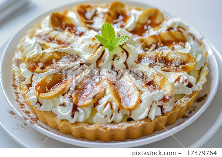 A luxurious caramel apple tart topped with whipped cream, chocolate shavings, and a sprinkle of powdered sugar, beautifully presented on a white plate.. A luxurious caramel apple tart topped with whipped cream, chocolate shavings, and a sprinkle of powdered sugar, beautifully presented on a white plate.. 117379764