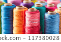 Close-up view of various colorful spools of thread arranged vertically, showcasing vibrant shades and textures for sewing projects.. 117380028