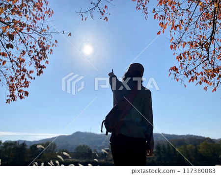 一個女人在秋葉中指著太陽的後視圖 一個女人在秋葉中指著太陽的後視圖 117380083