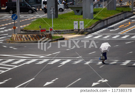 A person holding a parasol and crossing the street in a busy city center on a midsummer afternoon 117380378