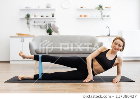 Woman exercising at home using resistance band on yoga mat 117380427