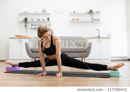 Woman practicing yoga split stretch at home on yoga mat 117380432