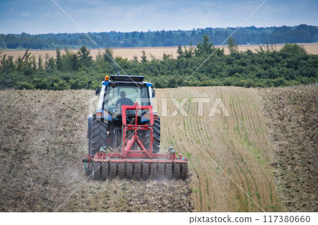 Tractor plowing a field in the countryside on a clear day with green forest in the background Tractor plowing a field in the countryside on a clear day with green forest in the background 117380660