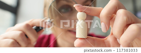 Woman looking at wooden person figure through magnifying glass Woman looking at wooden person figure through magnifying glass 117381033