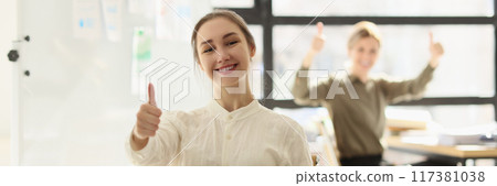 Smiling team of managers showing thumbs up sign and celebrating victory in office 117381038