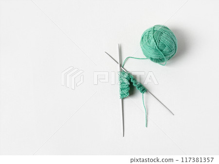 Green knitted wool on gray background with knitting needles for knitting warm clothes and hobbies needlework Green knitted wool on gray background with knitting needles for knitting warm clothes and hobbies needlework 117381357