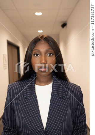 A confident businesswoman in a pinstripe suit embodies ambition and professionalism in a corridor 117381737