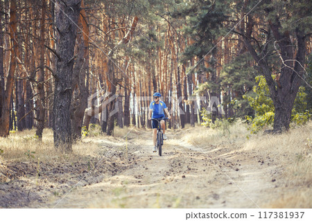 woman cyclist rides in the pine forest on a mountain bike. 117381937