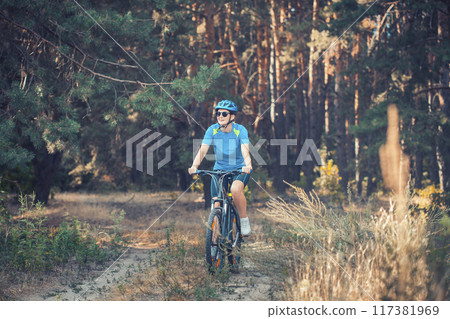 woman cyclist rides in the pine forest on a mountain bike. woman cyclist rides in the pine forest on a mountain bike. 117381969