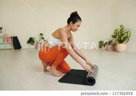 Woman Rolling Yoga Mat in Minimalistic Room 117382058