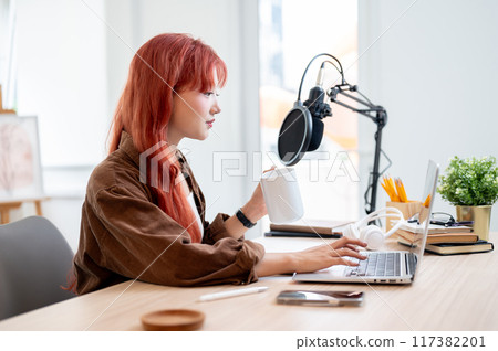 A beautiful Asian female podcaster is working in her home studio and enjoying a coffee. A beautiful Asian female podcaster is working in her home studio and enjoying a coffee. 117382201