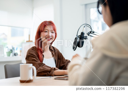 A friendly Asian female podcaster is enjoying a conversation as she interviews a guest in her studio A friendly Asian female podcaster is enjoying a conversation as she interviews a guest in her studio 117382206