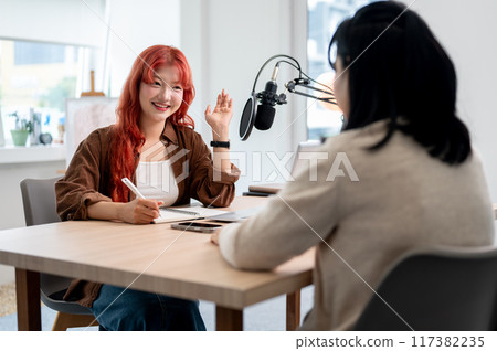 A beautiful Asian female podcaster is interviewing a guest, listening to their answers. 117382235