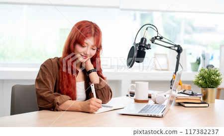 A beautiful Asian female podcaster is focusing on adjusting the script for the new podcast episode. 117382237