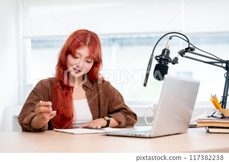 A beautiful Asian female podcaster is focusing on adjusting the script for the new podcast episode. A beautiful Asian female podcaster is focusing on adjusting the script for the new podcast episode. 117382238