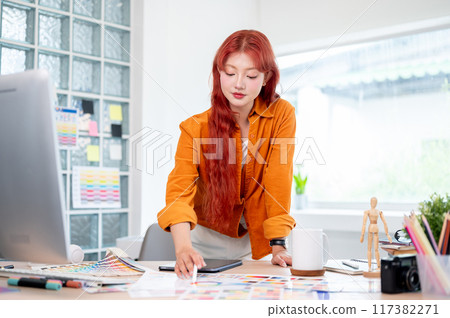 A graphic designer is focused on her new project, selecting colors from a set of swatches. 117382271