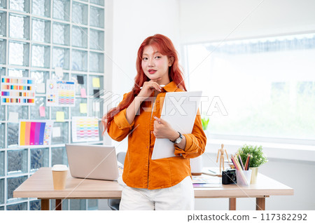 A confident female graphic designer stands in her studio with a graphic drawing tablet in her hand. A confident female graphic designer stands in her studio with a graphic drawing tablet in her hand. 117382292
