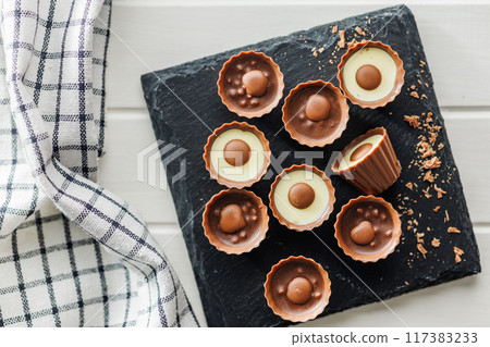 Sweet pralines. Chocolate truffles on cutting board on white table. Top view. Sweet pralines. Chocolate truffles on cutting board on white table. Top view. 117383233