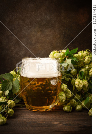 A mug of beer , on a wooden table, with a branch of fresh hops, rustic , no people, A mug of beer , on a wooden table, with a branch of fresh hops, rustic , no people, 117384412