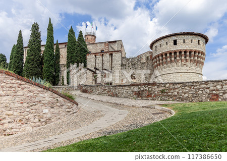 The imposing stone Brescia Castle in Italy, surrounded by cypress trees and serene historic pathways 117386650