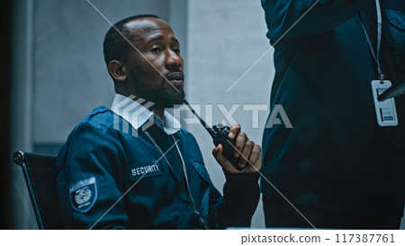 African American security officer talks in walkie talkie. Female coworker uses tablet 117387761