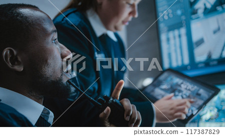 Female worker talks with security officer, uses tablet with surveillance footage Female worker talks with security officer, uses tablet with surveillance footage 117387829