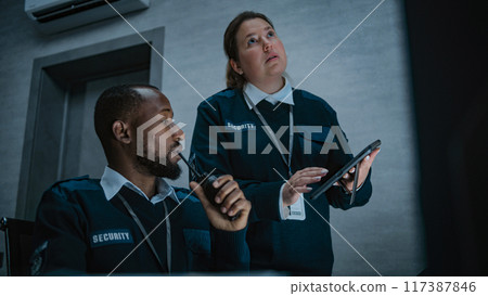 Female security officer stands and uses tablet. African American dispatcher talks in walkie talkie 117387846