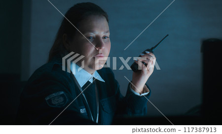 Female security officer uses walkie talkie sitting at workplace in monitoring center 117387913