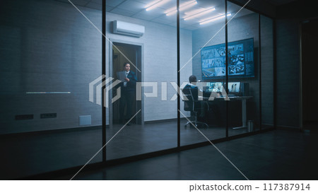 African American CCTV operator works on computer watching surveillance footage 117387914